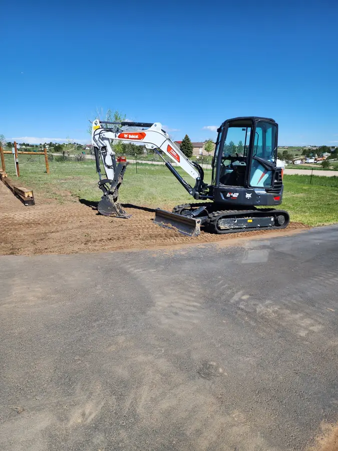 A mini excavator parked on a freshly graded dirt pad on the open plains under a blue sky
