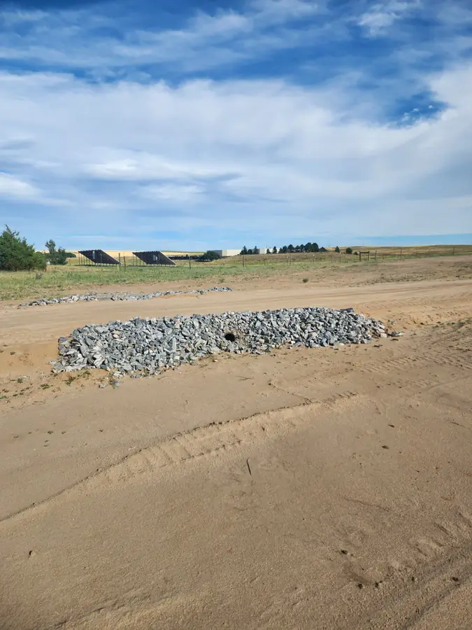 A pile of drainage rock on graded ground with the flat plains horizon behind it
