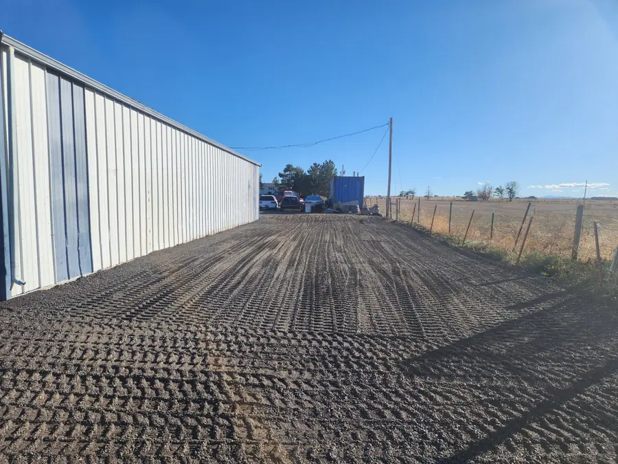 A wide graded gravel apron along a long white metal building