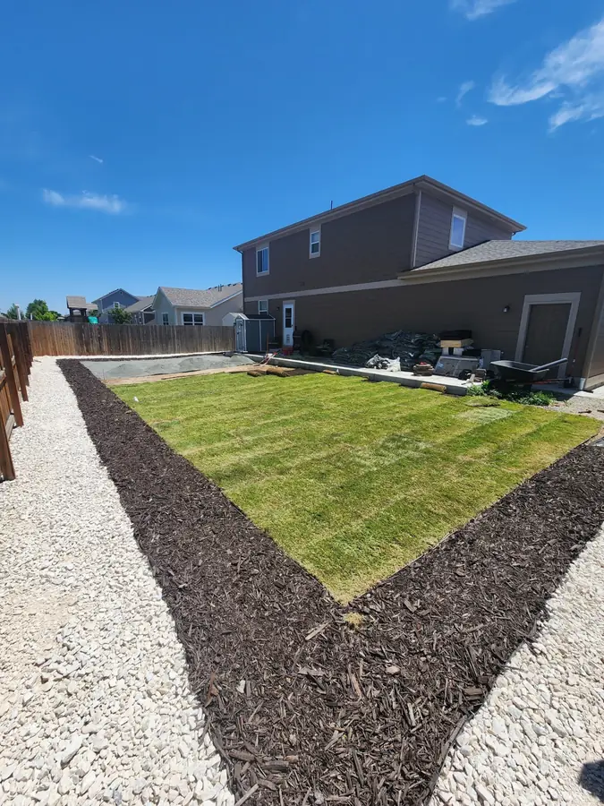 New sod edged with a mulch border and white rock beside a two-story house