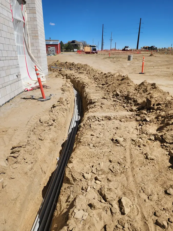 A utility trench with electrical conduit running along the side of a new house