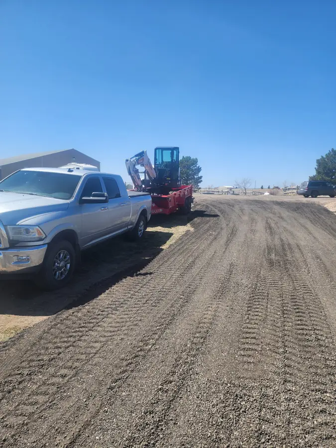 A pickup and a mini excavator on a freshly graded gravel driveway