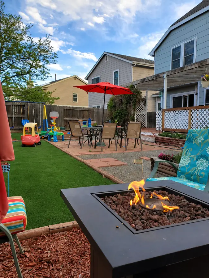 A finished backyard with artificial turf, a flagstone patio and a fire table