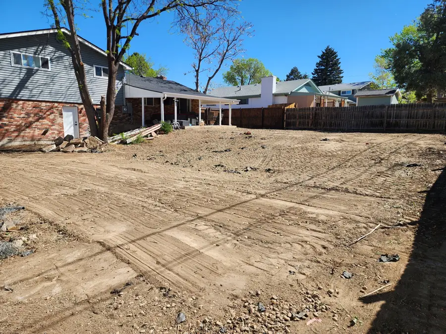 A backyard graded smooth and ready for finish work behind a brick house